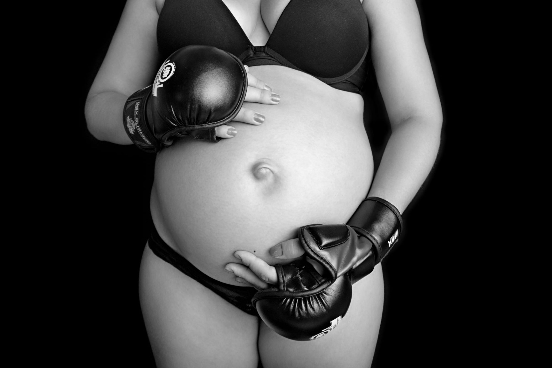 Černobílá fotografie z těhotenského focení. Těhotná má na sobě boxerské rukavice a černé pozadí. Domácí fotoateliér Mladá Boleslav.