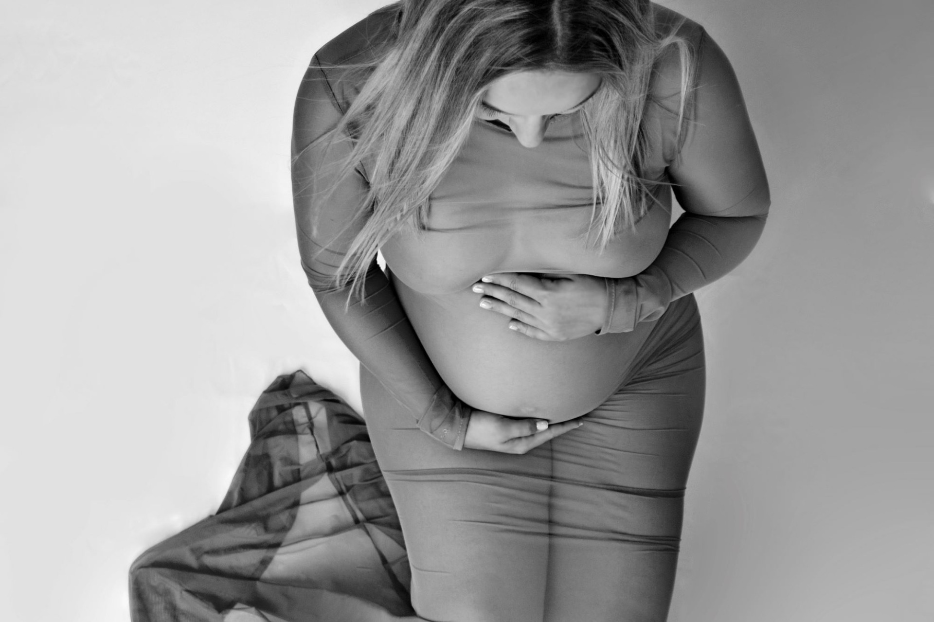 Černobílá fotografie z těhotenského focení. Těhotná má na sobě tělové šaty a bílé pozadí. Domácí fotoateliér Mladá Boleslav.