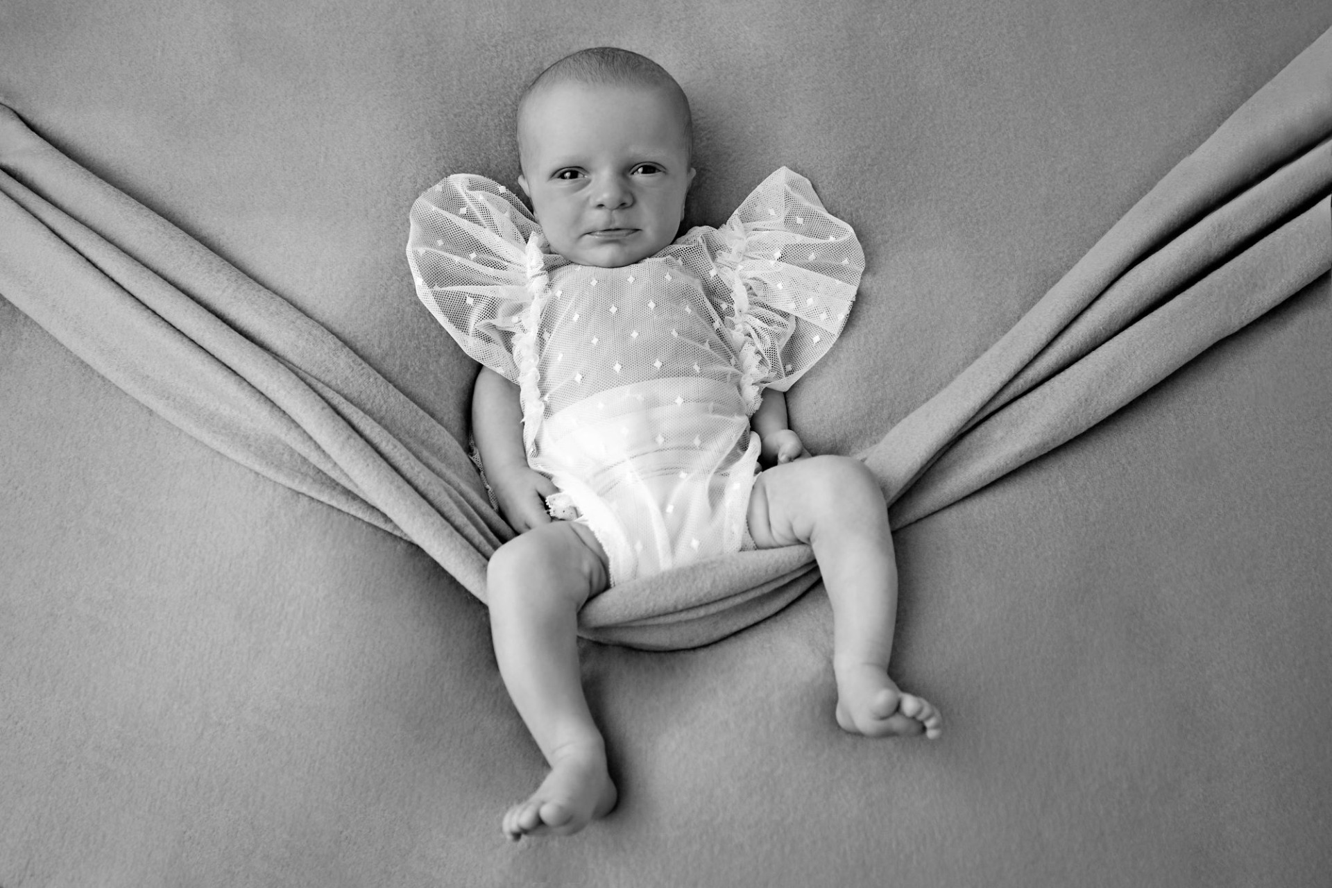 Černobílá fotografie z novorozeneckého, newborn focení. Několika denní miminko má na sobě bílé oblečení a šedé pozadí. Domácí fotoateliér Mladá Boleslav.