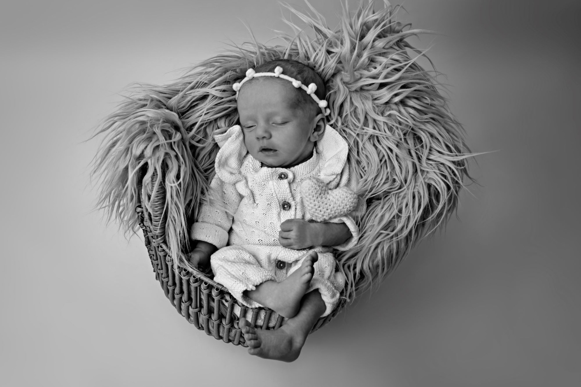 Černobílá fotografie z novorozeneckého, newborn focení. Několika denní miminko leží v košíku. Má na sobě bílé oblečení a bílé pozadí. Domácí fotoateliér Mladá Boleslav.