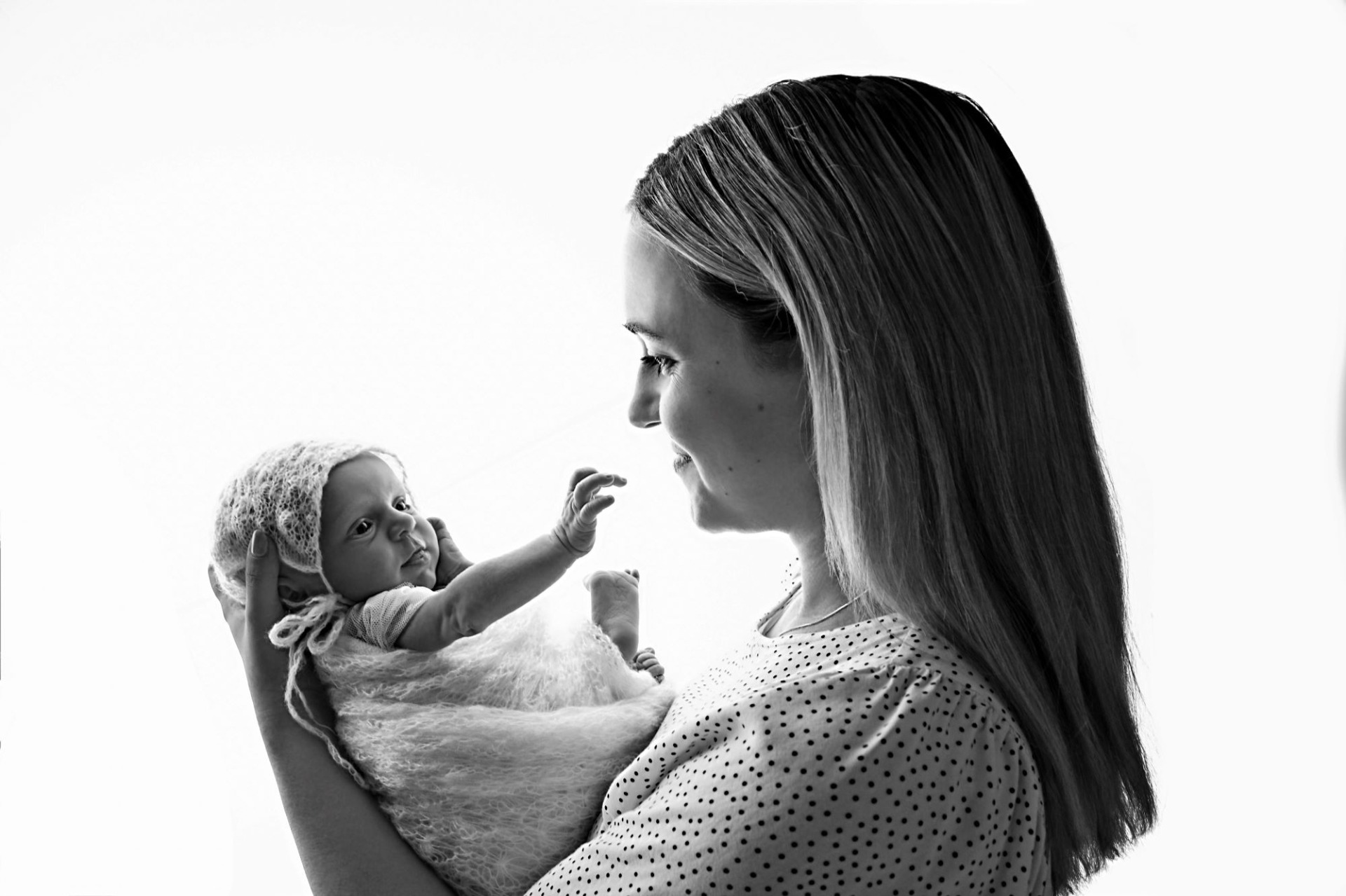Černobílá fotografie z novorozeneckého, newborn focení. Několika denní miminko drží jeho maminka v náručí. Foceno v protisvětle. Domácí fotoateliér Mladá Boleslav.